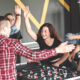 A diverse group of cheerful coworkers celebrating together while playing a game of foosball in a modern office environment.
