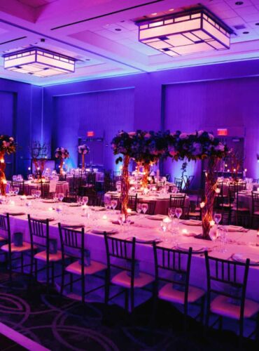 Elegant banquet hall set up for a corporate awards event with purple lighting, decorated tables, floral centerpieces, and candles.