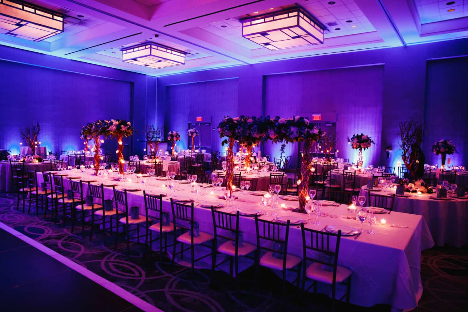 Elegant banquet hall set up for a corporate awards event with purple lighting, decorated tables, floral centerpieces, and candles.