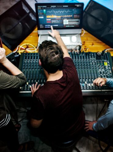 Team managing corporate event audio production using a sound mixing console, speakers, and live monitoring software during an event setup.