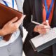 Two corporate event professionals in business attire reviewing documentation.