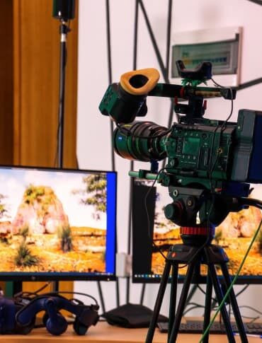 Professional video camera on a stand with monitors on a table.