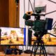 Professional video camera on a stand with monitors on a table.