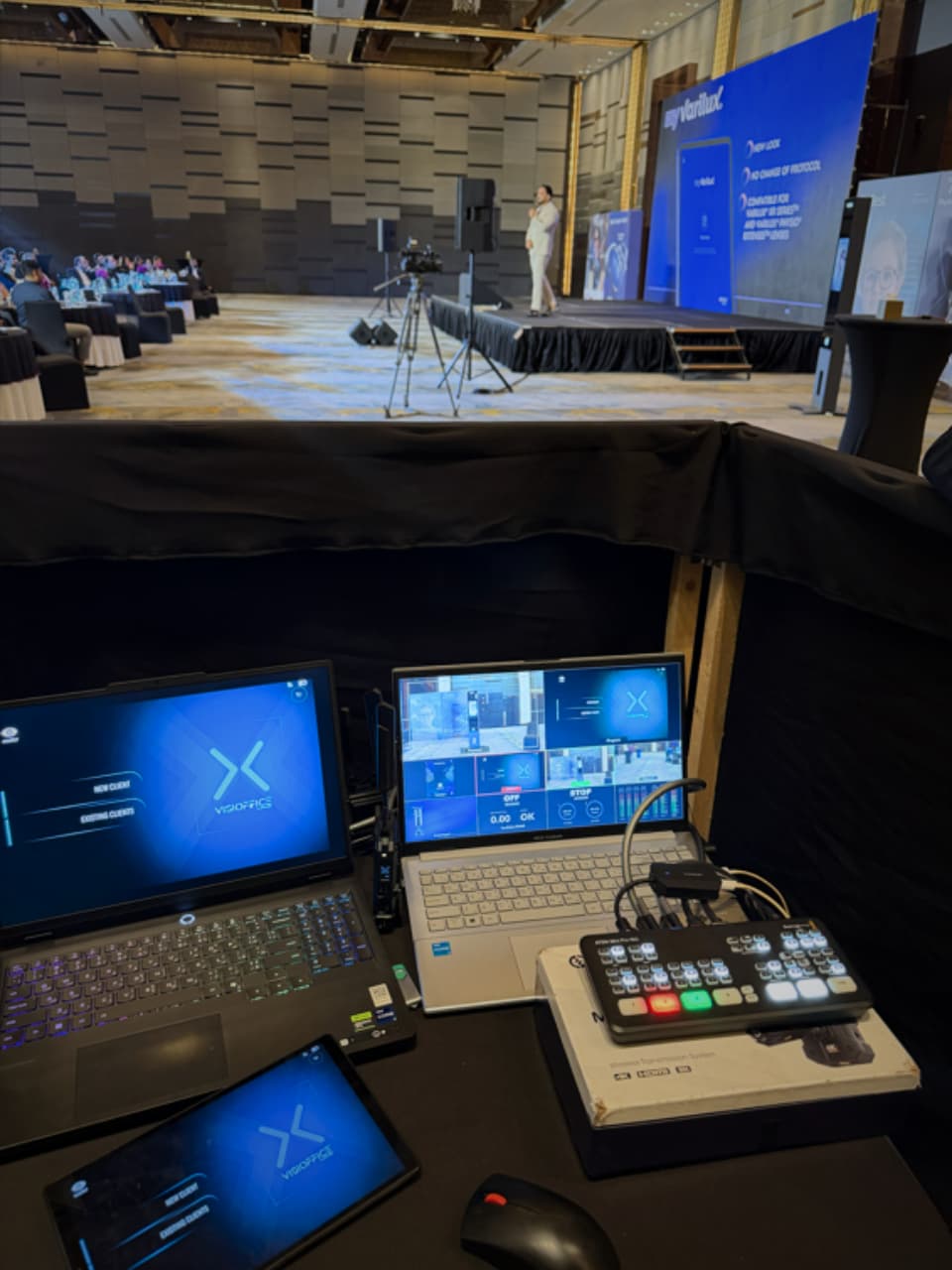 A behind-the-scenes view of a professional hybrid event setup in Dubai, featuring a video switcher and laptops monitoring a live stage presentation.