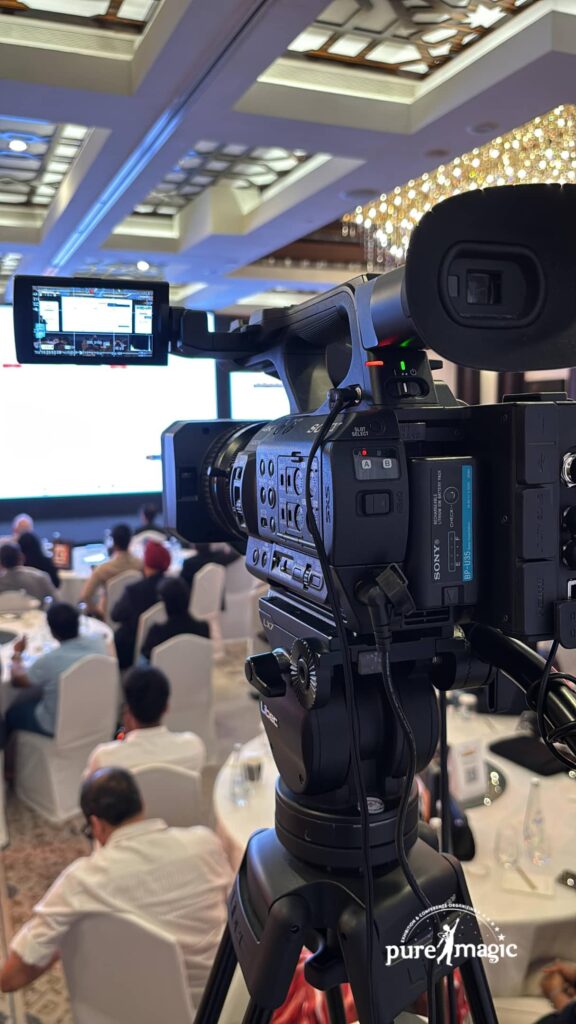 A professional broadcast-grade camera captures a corporate conference in a well-lit Dubai venue, showcasing the high-end equipment used for professional hybrid event production.